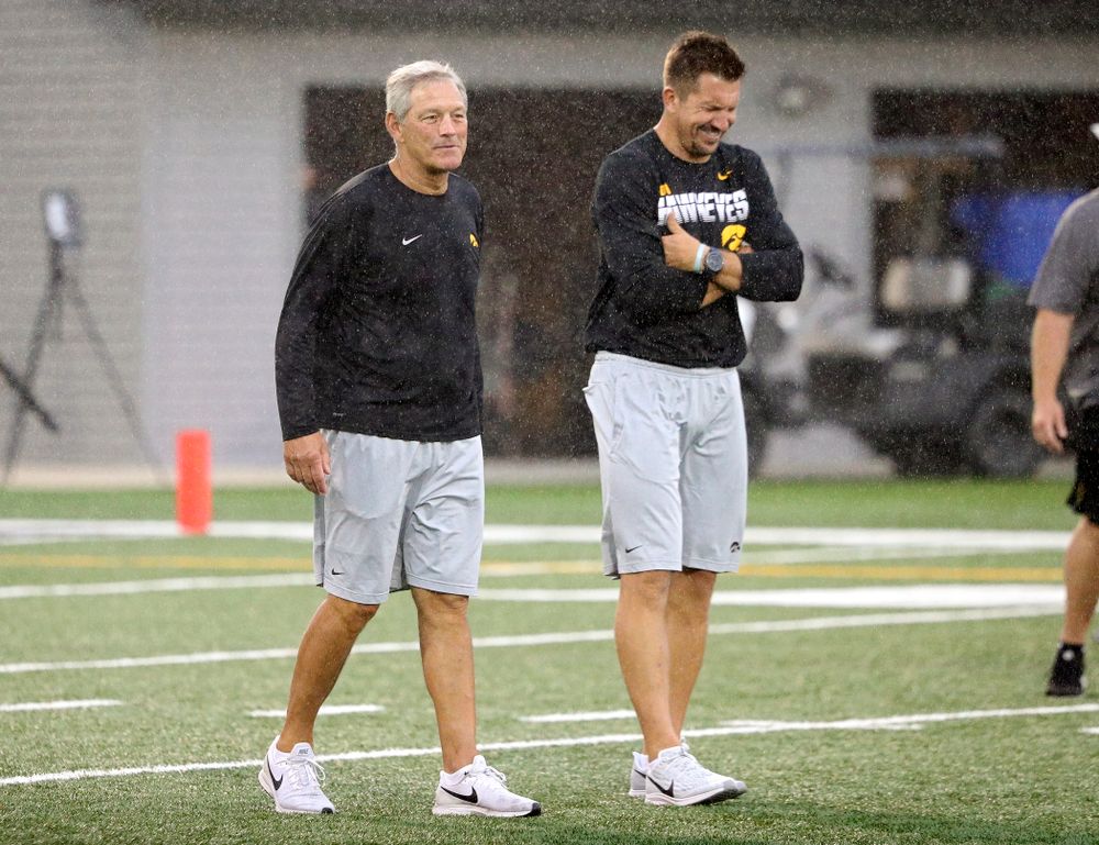 Iowa Hawkeyes head coach Kirk Ferentz talks with former Iowa Hawkeyes and Indianapolis Colts tight end Dallas Clark as rain falls durning Fall Camp Practice No. 17 at the Hansen Football Performance Center in Iowa City on Wednesday, Aug 21, 2019. (Stephen Mally/hawkeyesports.com)