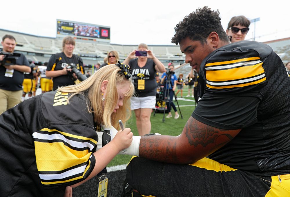 Kid Captain Kendra Hines signs the tape on the arm of Iowa Hawkeyes offensive lineman Tristan Wirfs (74) during Kids Day at Kinnick Stadium in Iowa City on Saturday, Aug 10, 2019. (Stephen Mally/hawkeyesports.com)